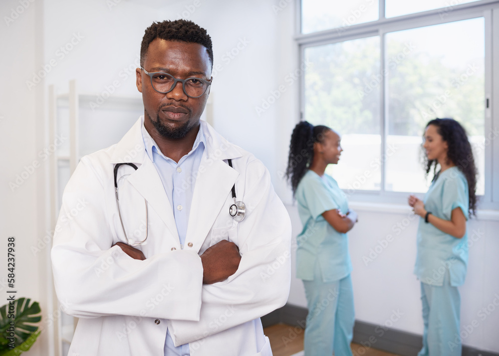 Portrait of serious doctor with arms folded, with two nurses in background