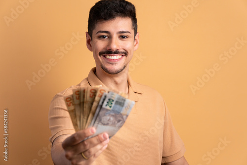 cheerful brazilian man showing money, brazilian currency in studio shot. business, loan, pay, wealth concept.  photo