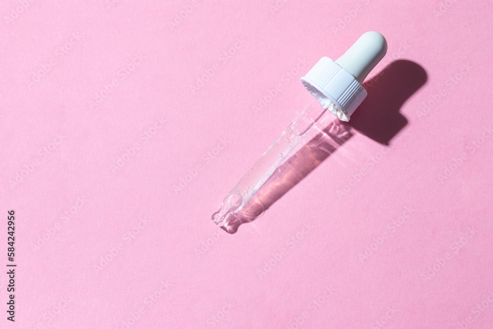 White dropper pipette with trasparent serum liquid, on pink background .Top view