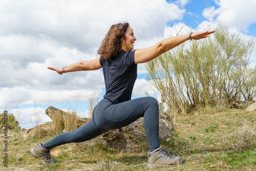 Woman practising yoga in the field, performing the warrior's pose. Woman practising yoga in the field, performing the warrior's pose.