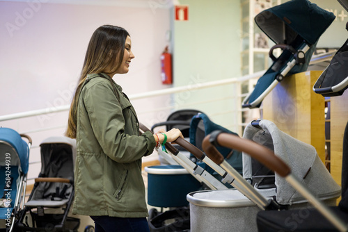 A pregnant Caucasian woman at a children's supply store. The adult girl tests the carts inside the store. Concept of choice for a baby stroller or stroller for newborns.