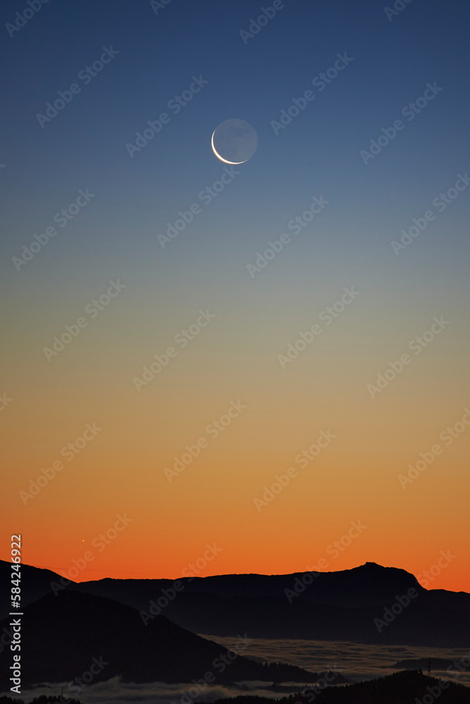 Luna creciente en el amanecer en un cielo azul y naranja