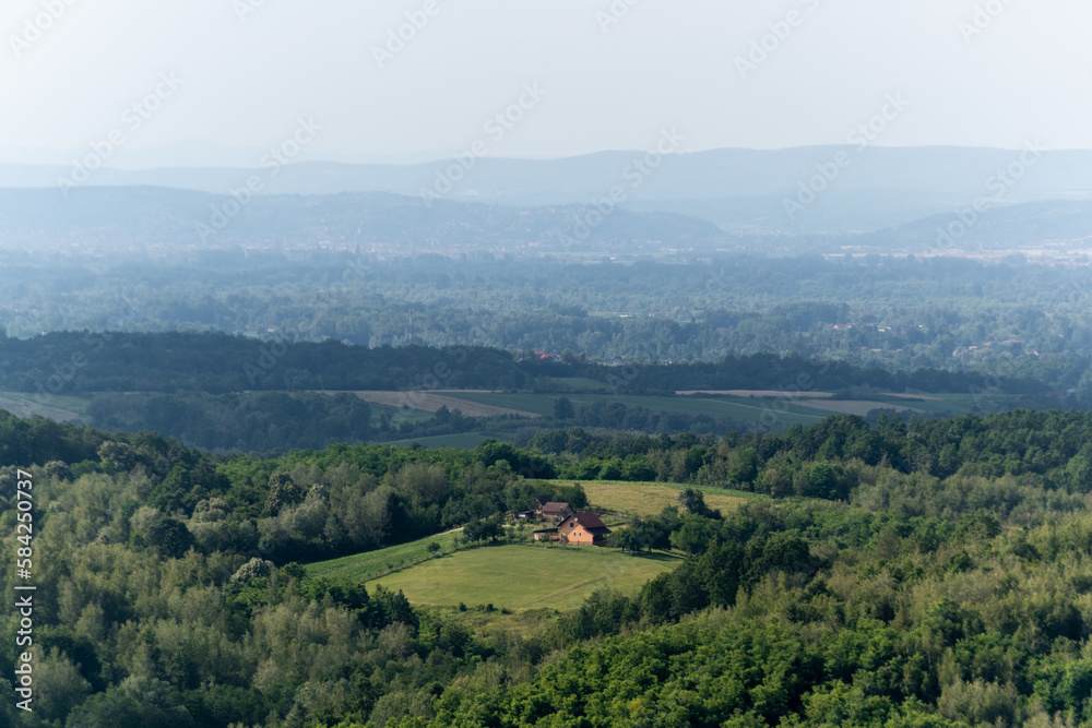 Rural house surrounded with lush forest, hill layers in haze