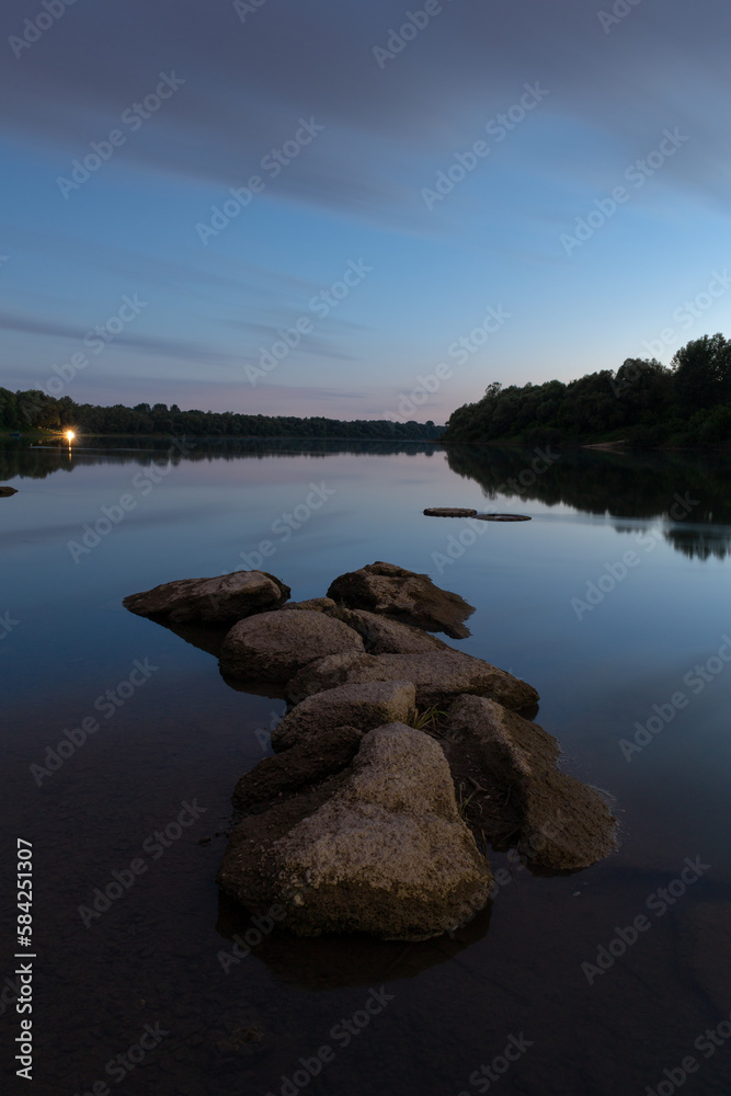 Boulders in river at blue hour, calm river landscape in long exposure with cloudy sky