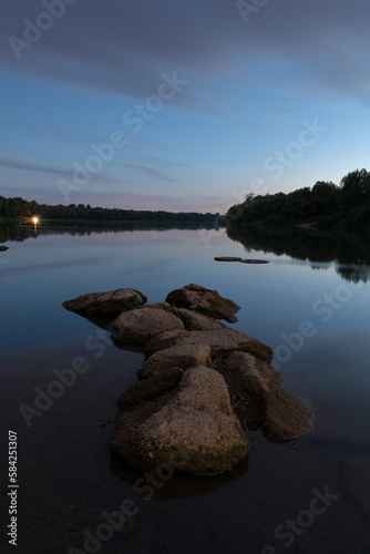Boulders in river at blue hour, calm river landscape in long exposure with cloudy sky