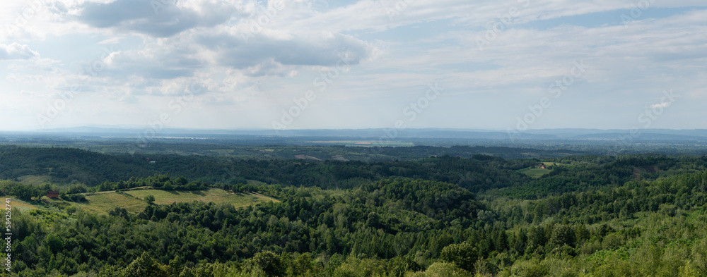 Hilly countryside panorama, distant valley filled with haze, scattered village and lush forests