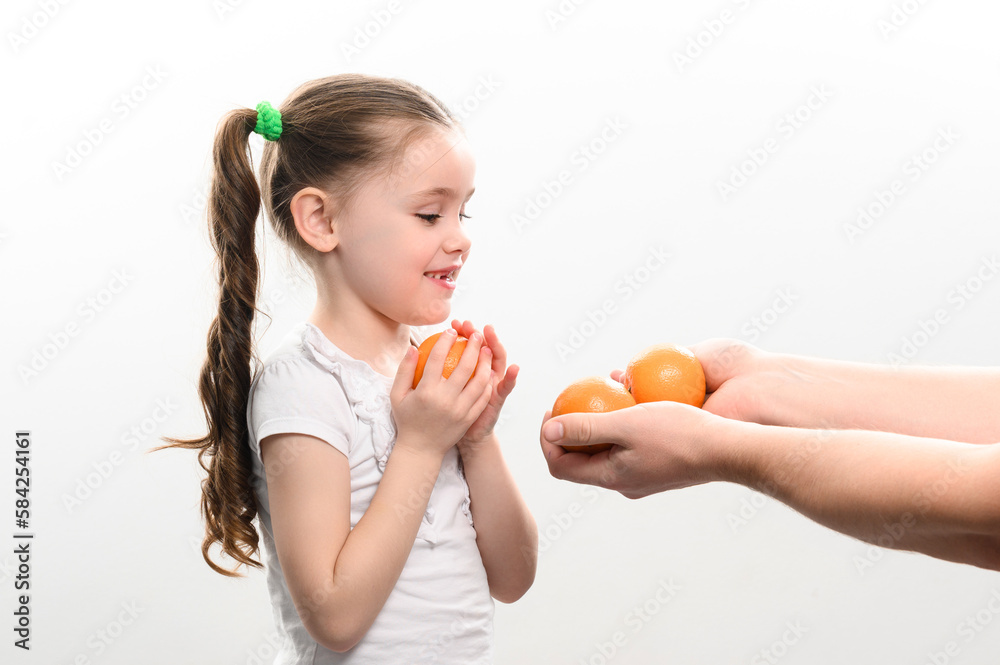A little girl is given tangerines on a white background, the child takes tangerines. A little girl is given tangerines on a white background, the child takes tangerines.