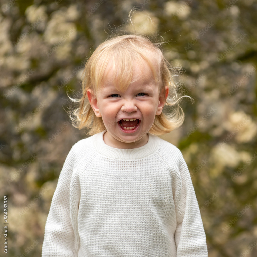 Cute blonde kid smiling outside in a park. Happy kid playing outside on a spring day. Adorable caucasian child walking in a garden, looking and smiling at the camera. Cute blonde kid smiling outside in a park. Happy kid playing outside on a spring day. Adorable caucasian child walking in a garden, looking and smiling at the camera.