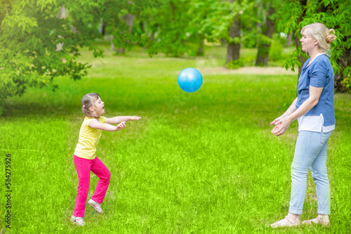 Little girl with syndrome down and her mother play with a ball in a summer park