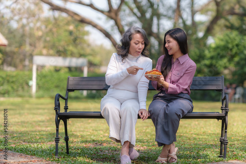 Asian mother and daughter sitting in the park happily and warmly eat food and bread together