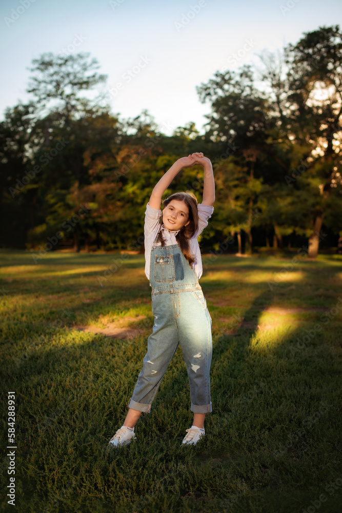 Fototapeta premium child girl walking outdoors and warm-up for her back and arms after classes in school yard. Copy space vertical photo