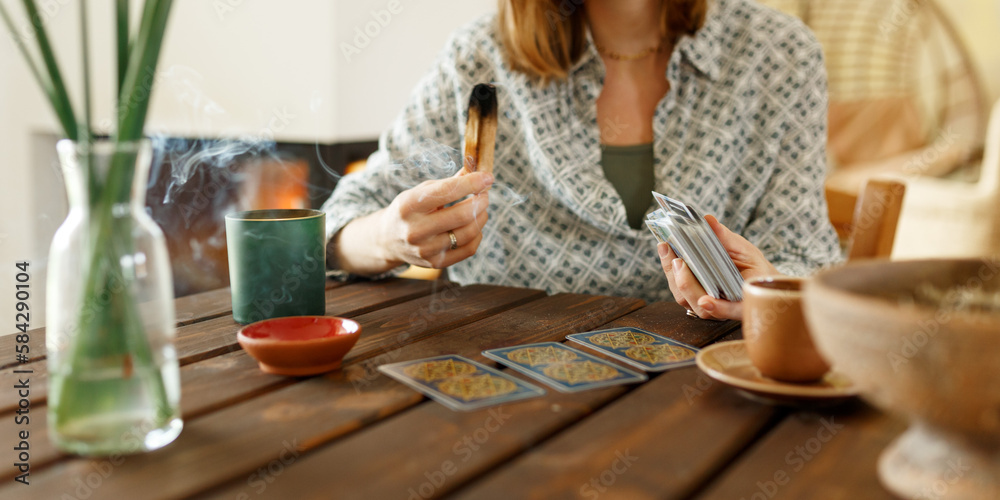 Fortune teller with tarot cards on table near burning candle.Tarot cards spread on table with magic herbs and palo santo aroma sticks. Forecasting concept Fortune teller with tarot cards on table near burning candle.Tarot cards spread on table with magic herbs and palo santo aroma sticks. Forecasting concept