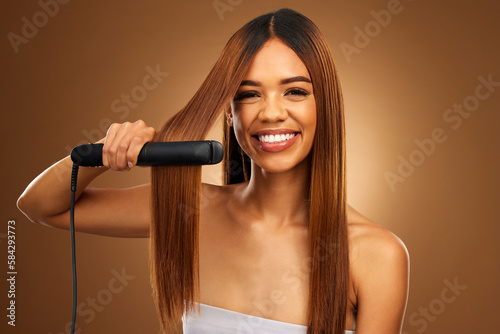Hair care, portrait of woman with hot iron and smile for luxury salon treatment on brown background. Beauty, haircut and happy hispanic model with straight hairstyle in studio for haircare styling.