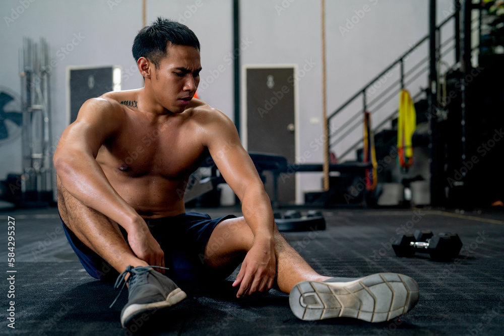 Obraz premium Front view of Asian sport man with shirtless sit on floor of fitness gym after finish of exercise.