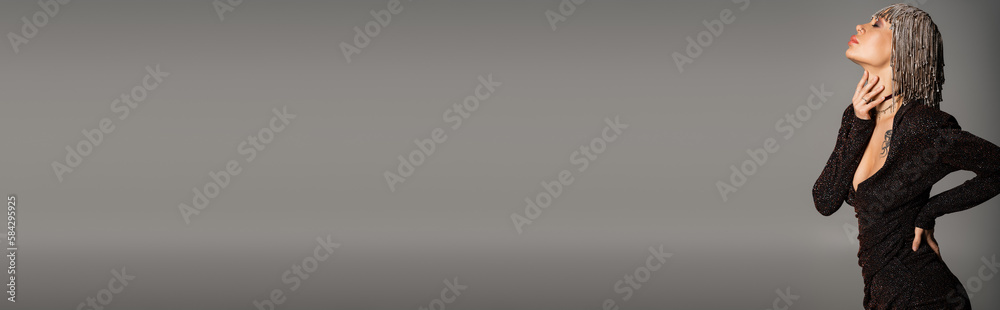 Fototapeta premium side view of sensual woman in black dress and shiny jewelry headwear touching neck isolated on grey, banner.