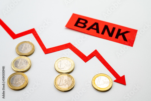 Rows of coins of descending height, descending red line, and the word Bank. Failure of banks and collapse of stock exchanges and yields.
