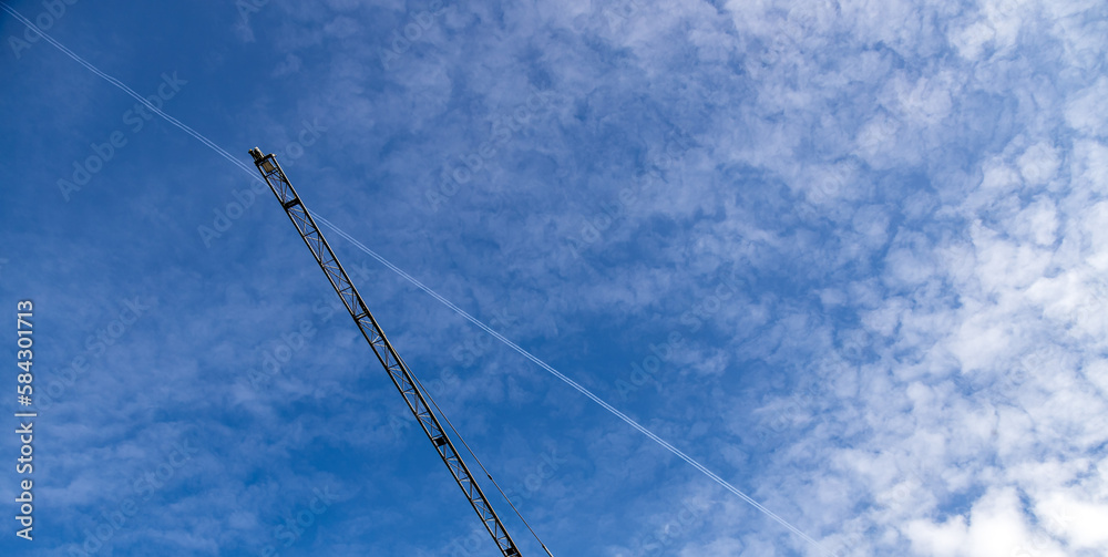 Beautiful view of blue sky with clouds, jet trail and a crane machinery seen in Piove di Sacco, Veneto, Italy Beautiful view of blue sky with clouds, jet trail and a crane machinery seen in Piove di Sacco, Veneto, Italy