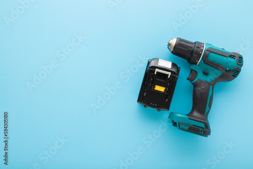 Cordless dark black green professional screwdriver with battery on light blue table background. Pastel color. Closeup. Tool for repair work. Top down view. Empty place for text.