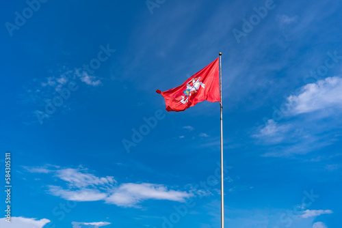 The historic flag of Lithuania, a rider with a sword on a white horse on a red background flutters against a bright blue sky with white clouds photo