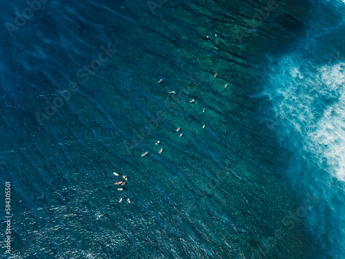 Surfers in transparent ocean. Surfing spot in tropical island. Aerial view.
