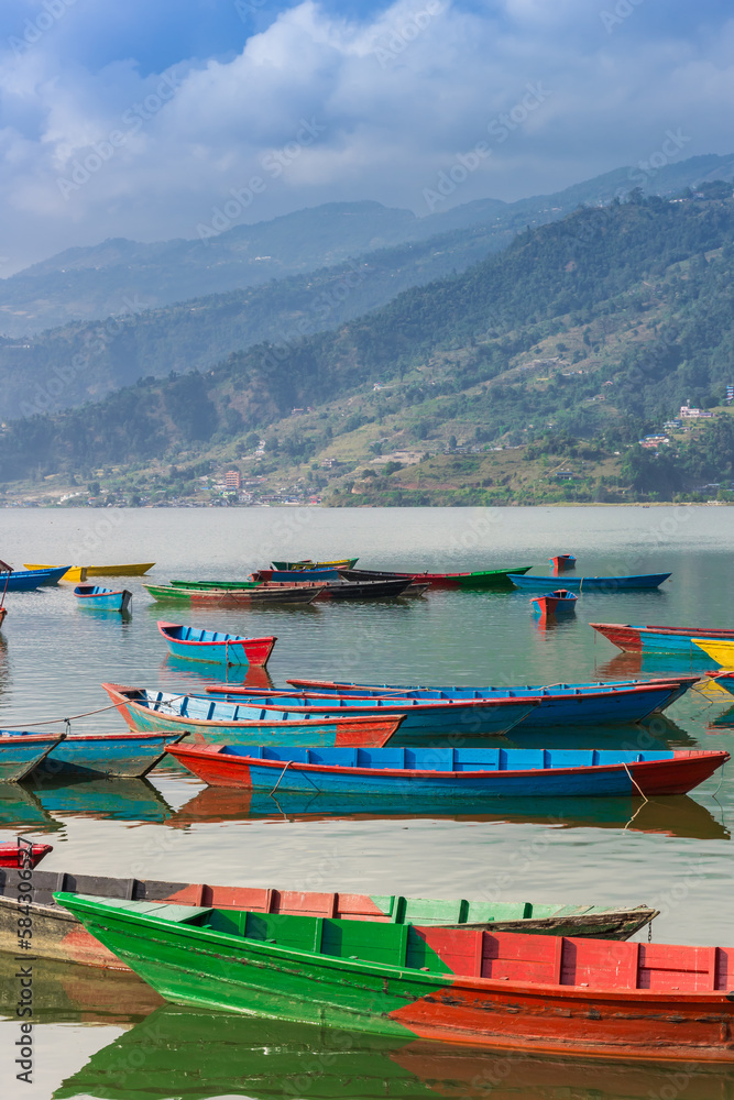 Colorful wooden boats with mountain backdrop at lake Phewa in Pokhara, Nepal