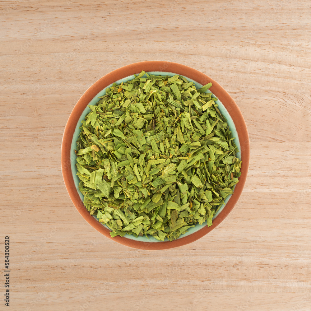 Overhead view of cut tarragon in a small terracotta bowl on a wood tabletop. Overhead view of cut tarragon in a small terracotta bowl on a wood tabletop.