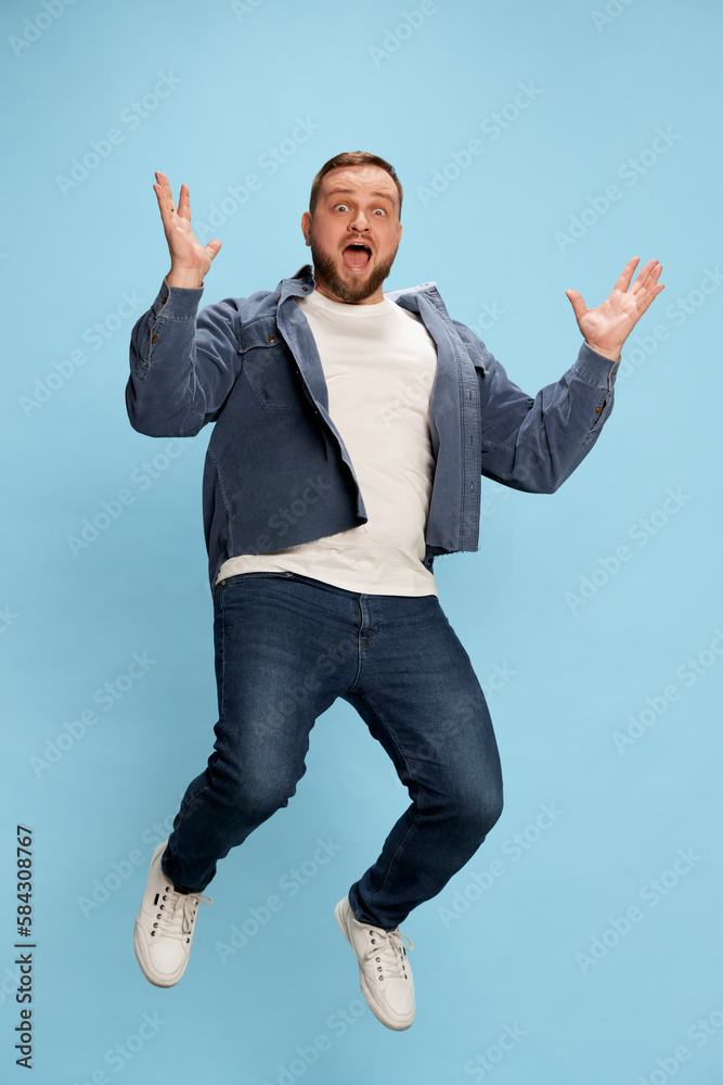 Handsome jumping man wearing white t-short spreading hands and smiling at camera over blue background
