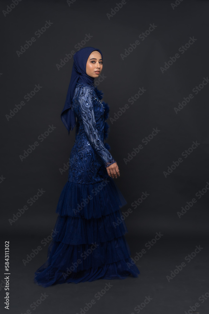 A teenager model use blue dress. She's pose in the studio indoor. She's pose in dark gray background with elegant pose. She's look like beautiful and graceful	
