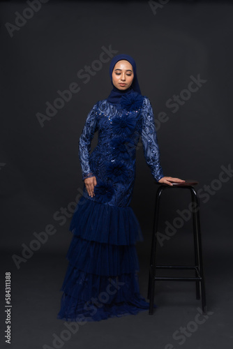 A teenager model use blue dress. She's pose in the studio indoor. She's pose in dark gray background with elegant pose. She's look like beautiful and graceful	 photo