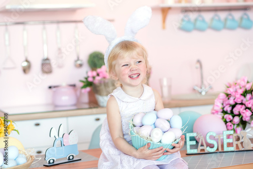 Cute little girl with bunny ears holding Easter egg in the kitchen decorated for Easter. © Maryna