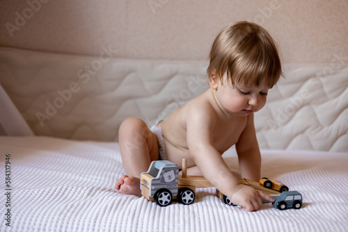A baby sits on a bed with a toy car and a wooden car.