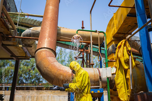 Male workers dressing in protective shower detoxification suit clean up after sealing a leaking container from corrosive toxic