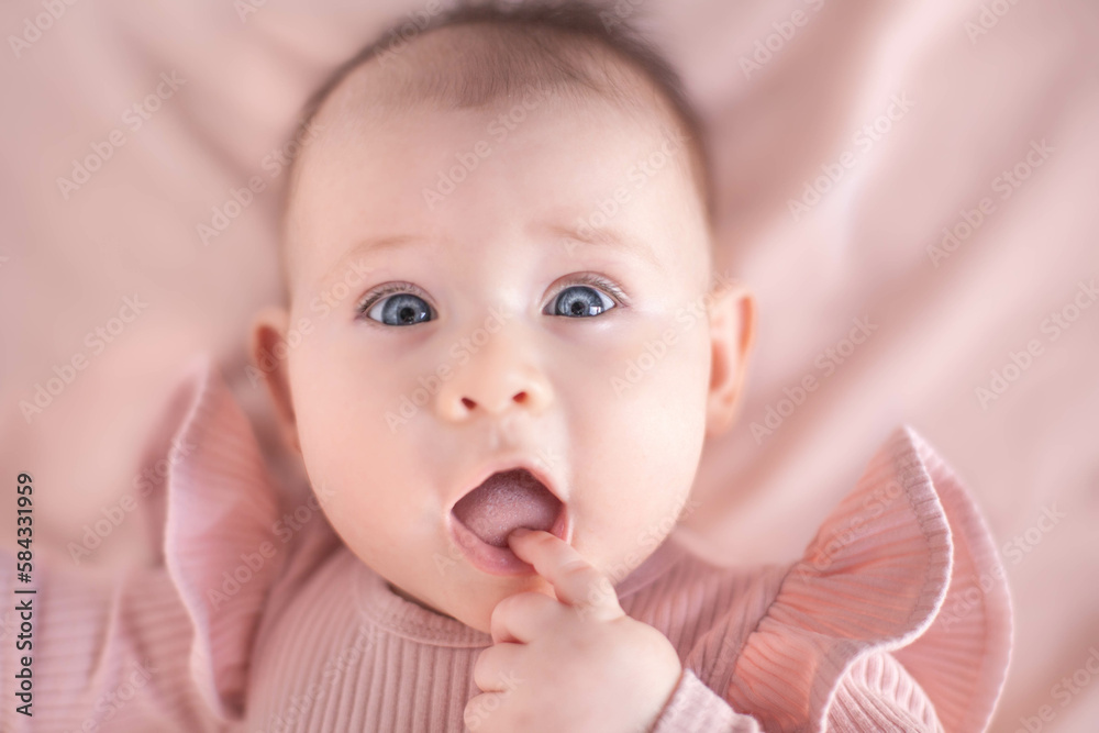 Portrait of a blue-eyed 6 months baby girl with finger in mouth