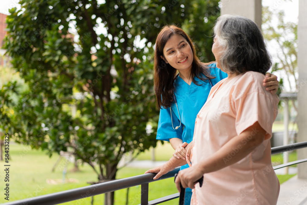 Asian careful caregiver or nurse hold patient hand and encourage patient, walking in garden. Concept of happy retirement with care from a caregiver and Savings and senior health insurance.