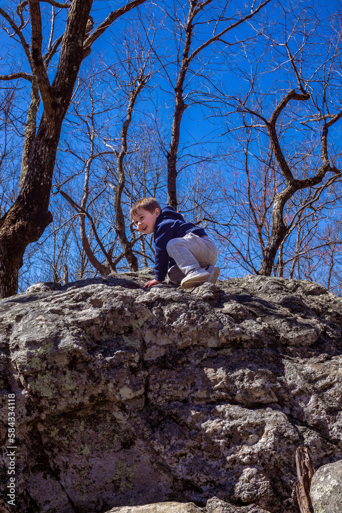 Young toddler boy crawling along rock boulders while hiking up Cheaha mountain in Alabama state park and campground Young toddler boy crawling along rock boulders while hiking up Cheaha mountain in Alabama state park and campground