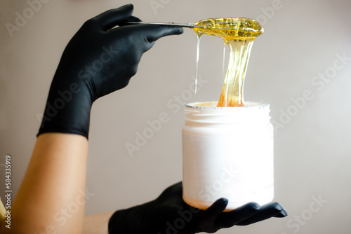 A female beautician holds a jar of shugaring sugar waxing paste, a light-coloured background. photo