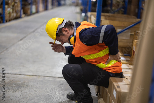 The warehouse worker suffered from a back injury while lifting and carrying heavy gear and keeping a twisted posture. Muscles can get strained, overused through continuous, repetitive movements. photo