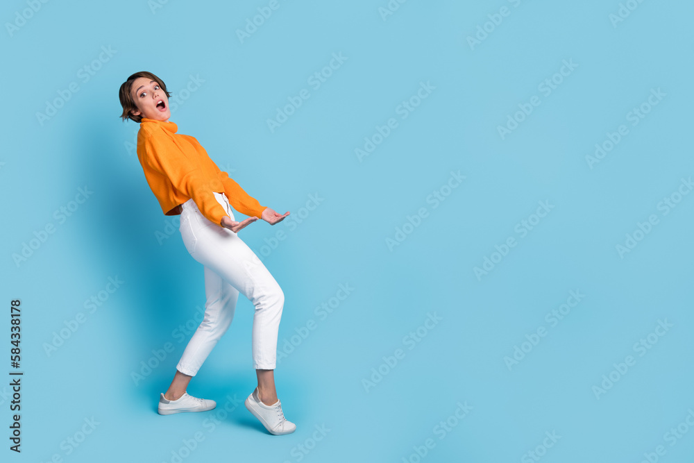 Full body photo of funky young woman carry heavy invisible box empty space dressed stylish orange look isolated on blue color background Full body photo of funky young woman carry heavy invisible box empty space dressed stylish orange look isolated on blue color background