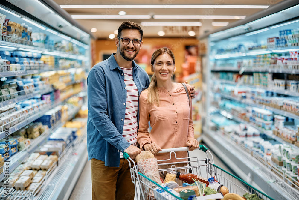 Happy couple shopping in supermarket and looking at camera.