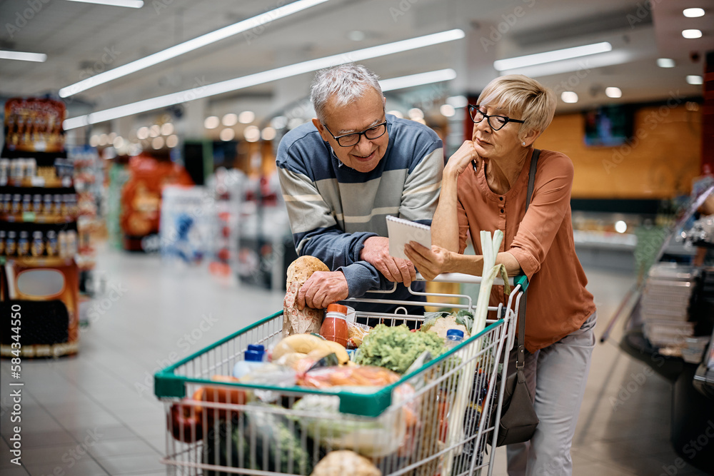 Senior couple going through shopping list while buying groceries in supermarket.