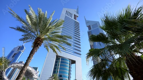 4K wide angle video with palm trees and Emirates Towers landmark skyscraper buildings in Dubai, 2023.