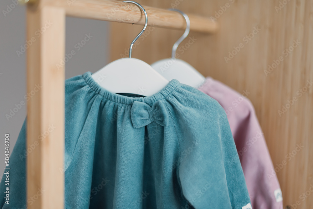 Blue, pink dresses for baby girl on white hanger in nursery. Set of baby clothes and accessories for birthday party. Fashion childs outfit. Copy space Blue, pink dresses for baby girl on white hanger in nursery. Set of baby clothes and accessories for birthday party. Fashion childs outfit. Copy space