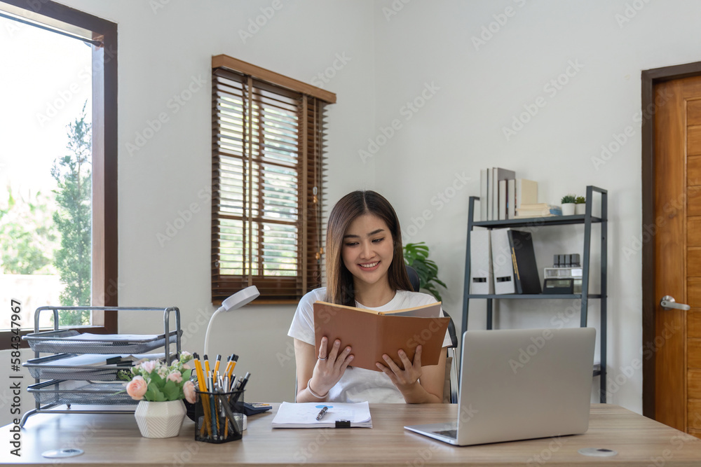 Asian business woman using computer for working and a read report book at home.