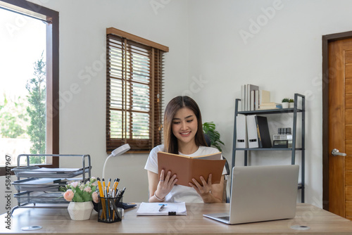 Asian business woman using computer for working and a read report book at home.