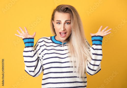 Amused young woman with opened hands, isolated on yellow background. Yes concept. Good news. Amusing girl celebrates success