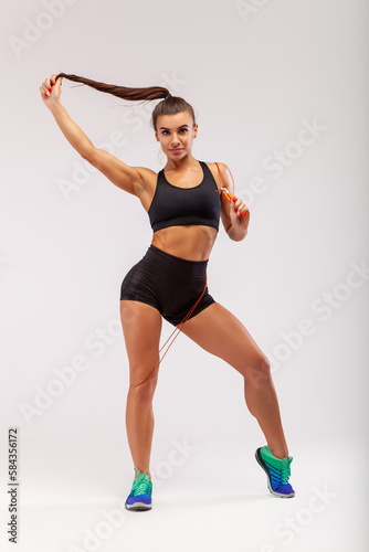 Sporty girl exercising with skipping rope. Photo of girl in black sportswear on white background. Dynamic movement. Full length. Sports and healthy lifestyle. skipping rope