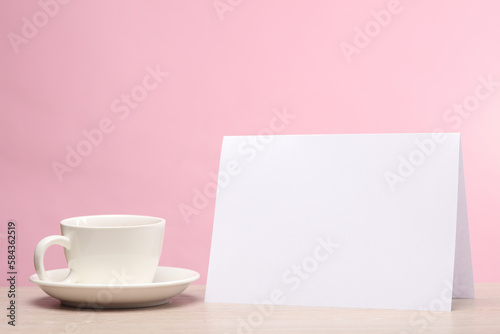 Coffee cup with blank white paper calendar or table flyer mockup on pink background