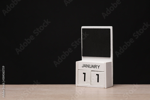 White wooden block monthly calendar with the date january 11 on the table, black blackbackground. Planning