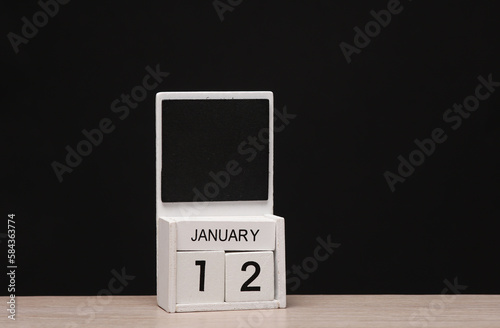 White wooden block monthly calendar with the date january 12 on the table, black blackbackground. Planning