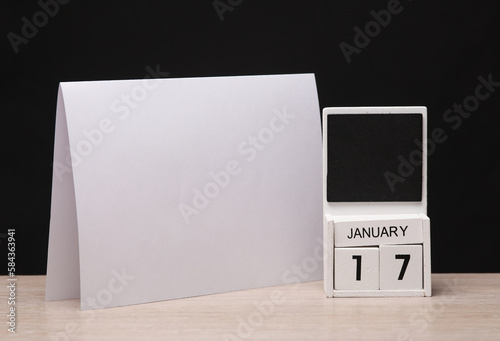 White wooden block monthly calendar with the date january 17 and table flyer mockup on the table, black blackbackground. Planning